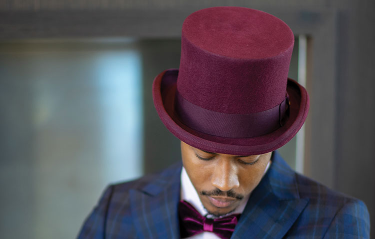 Man wearing a rosy red top hat and blue suit looking downwards