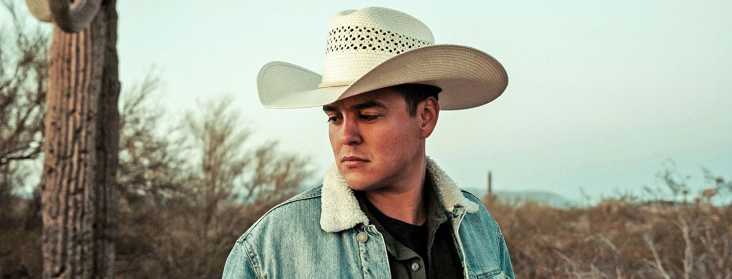 Man wearing a denim jacket with white hat in a dry field
