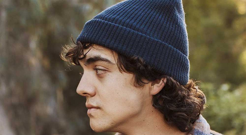 Man wearing a blue beanie with his brown curly hair flaired out from underneath
