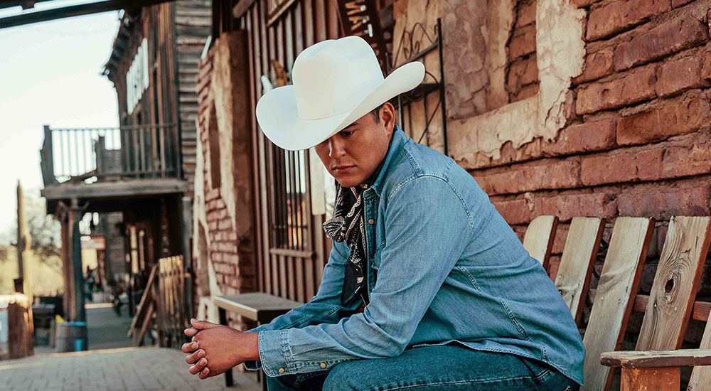 Man wearing a white cowboy hat and levi jacket looking downward in contemplation