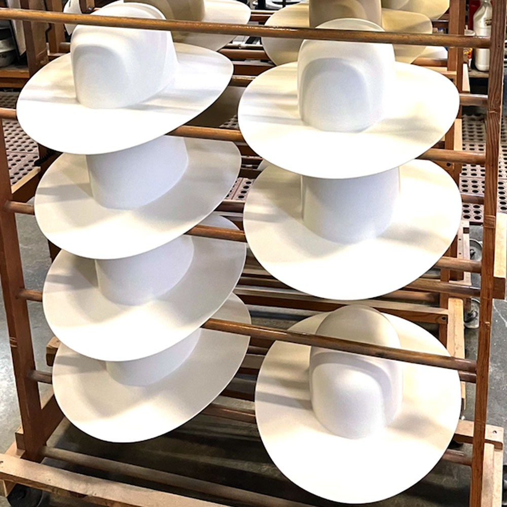 White cowboy hats resting on a rack after getting pressed into shape