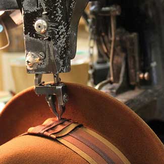 A brown hat having a sewing machine attach the dark colored band above the brim